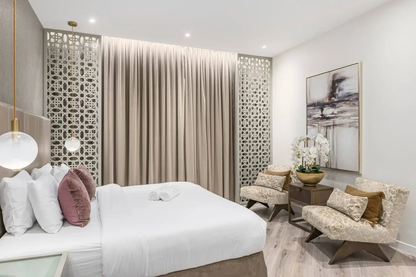 A bright bedroom with a white bed, patterned screens, and a seating area.