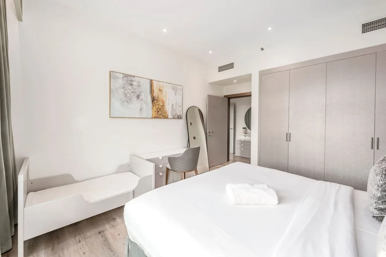 A bright bedroom with a white bed, built-in wardrobes, and a desk.