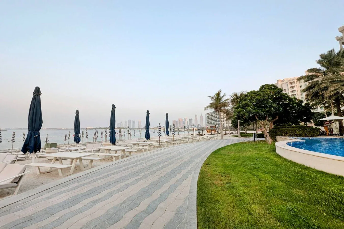 A landscaped waterfront promenade with shaded seating and a pool.