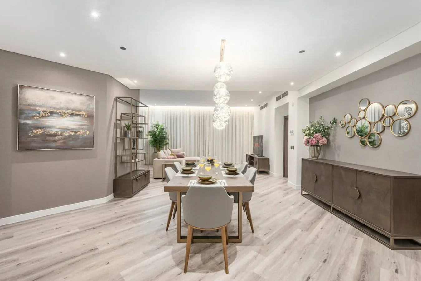 A bright dining room with a long table, chairs, and a hanging chandelier.