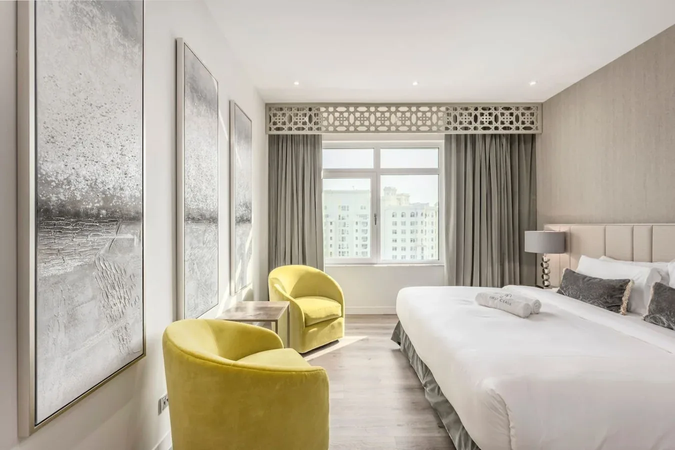 A bright bedroom with a large bed, yellow seating, and a window.