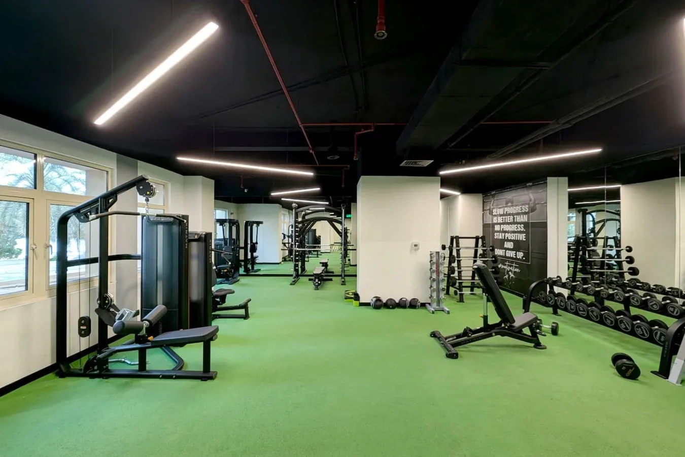 A gym with exercise machines, free weights, and green flooring.