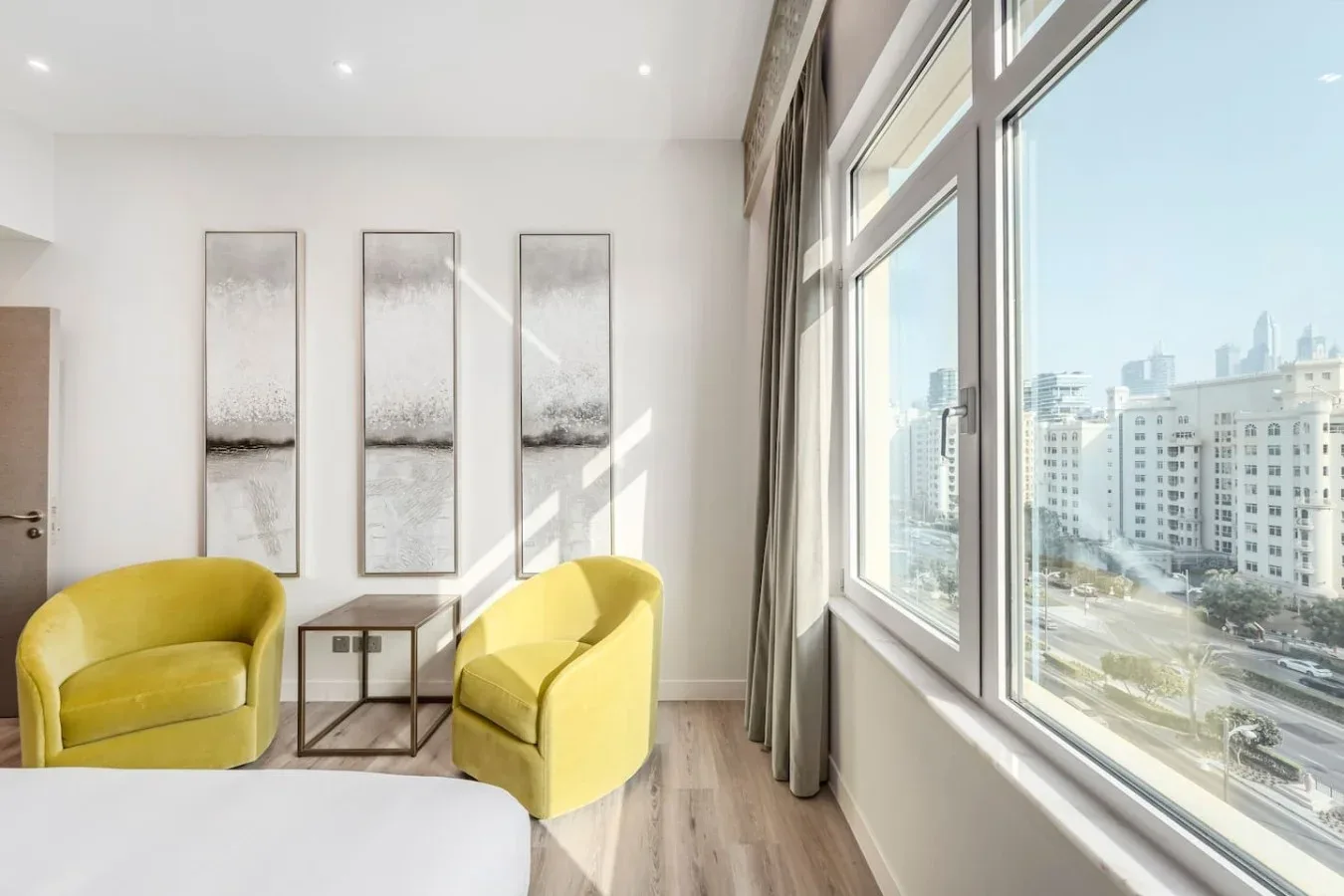 A bright sitting area with yellow seating beside large windows overlooking city buildings.