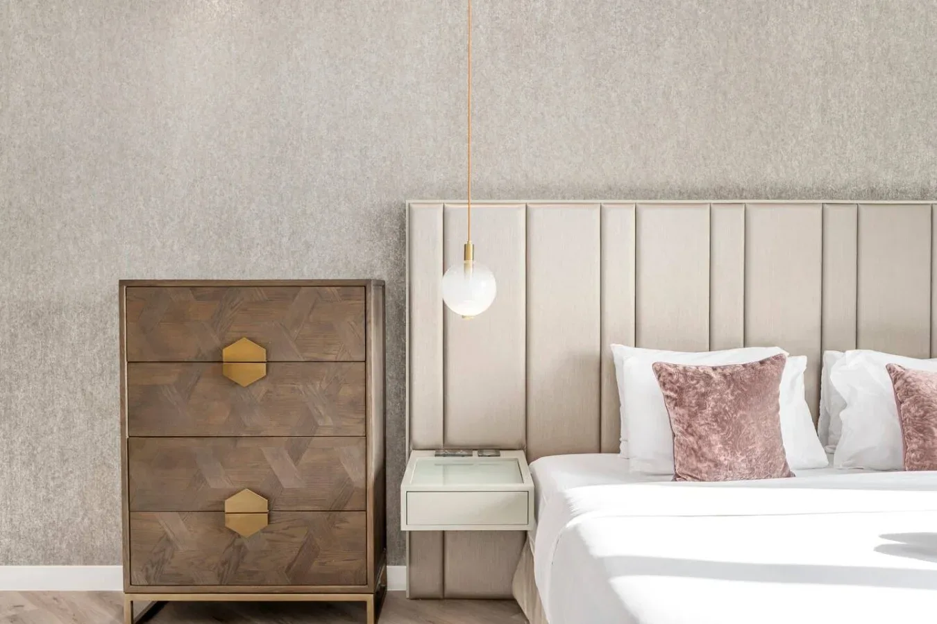 A bedroom with a bed, upholstered headboard, and wooden chest of drawers.
