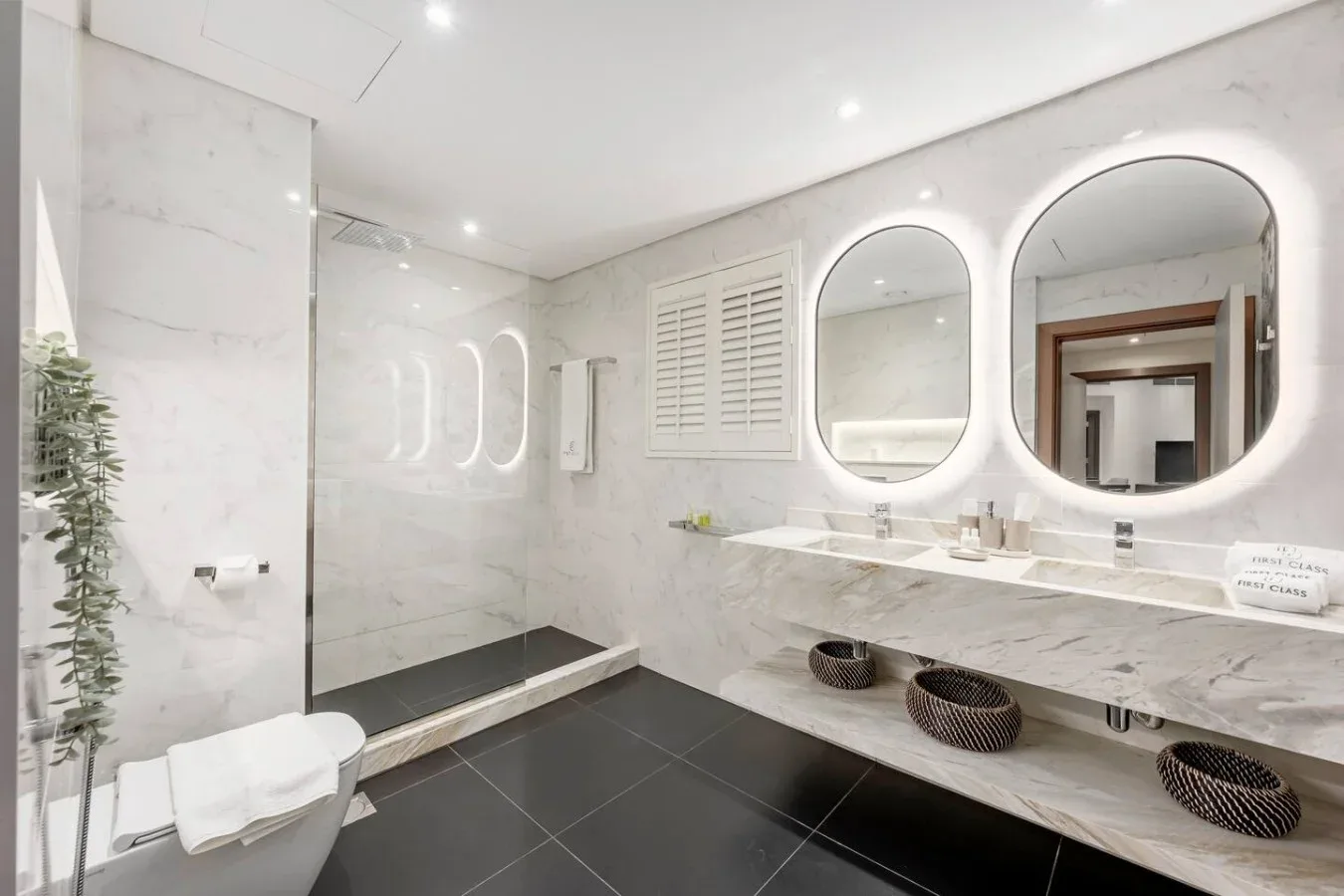 A bright bathroom with a long vanity, mirrors, and a walk-in shower.