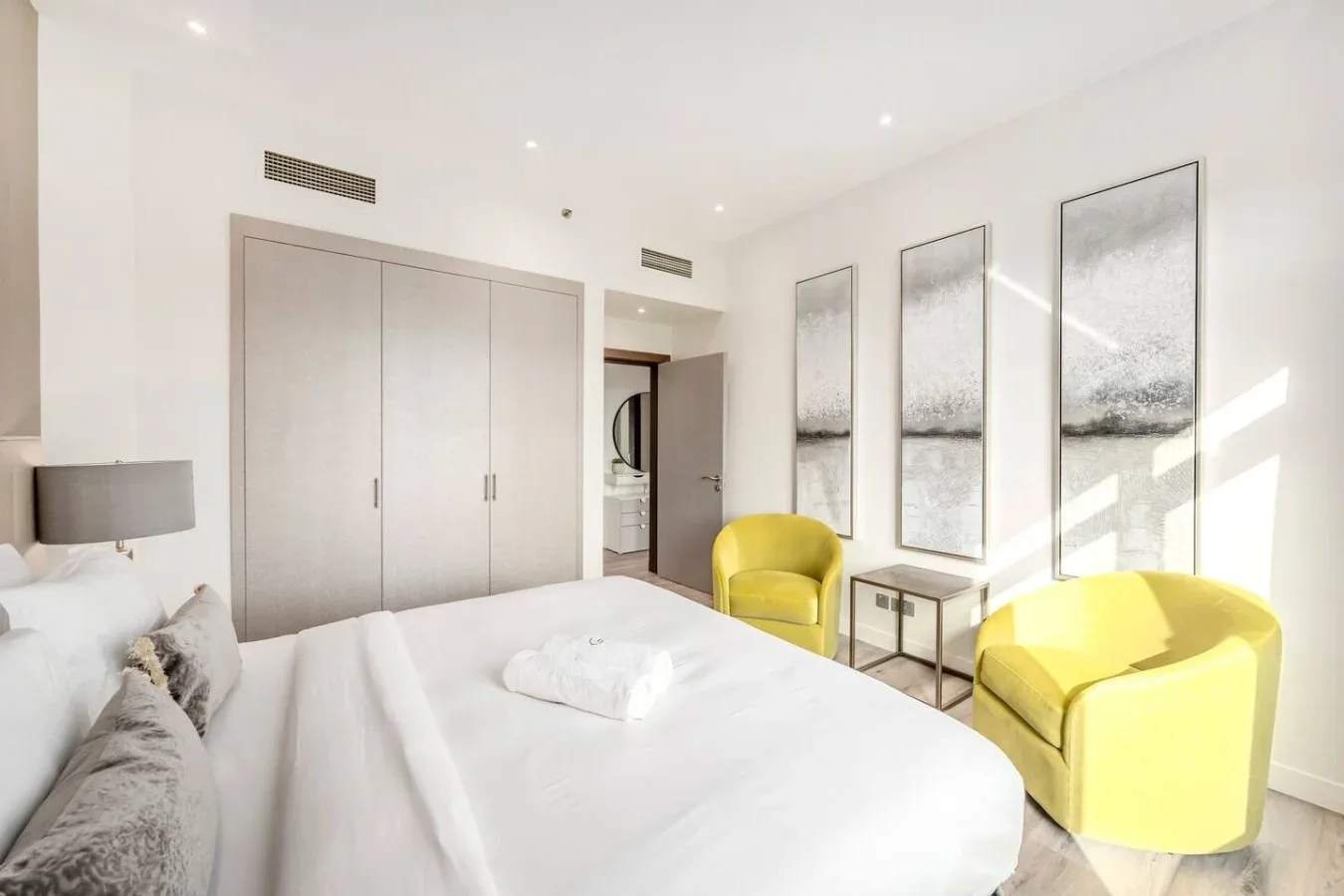 A bright bedroom with a neatly made bed and two yellow armchairs.