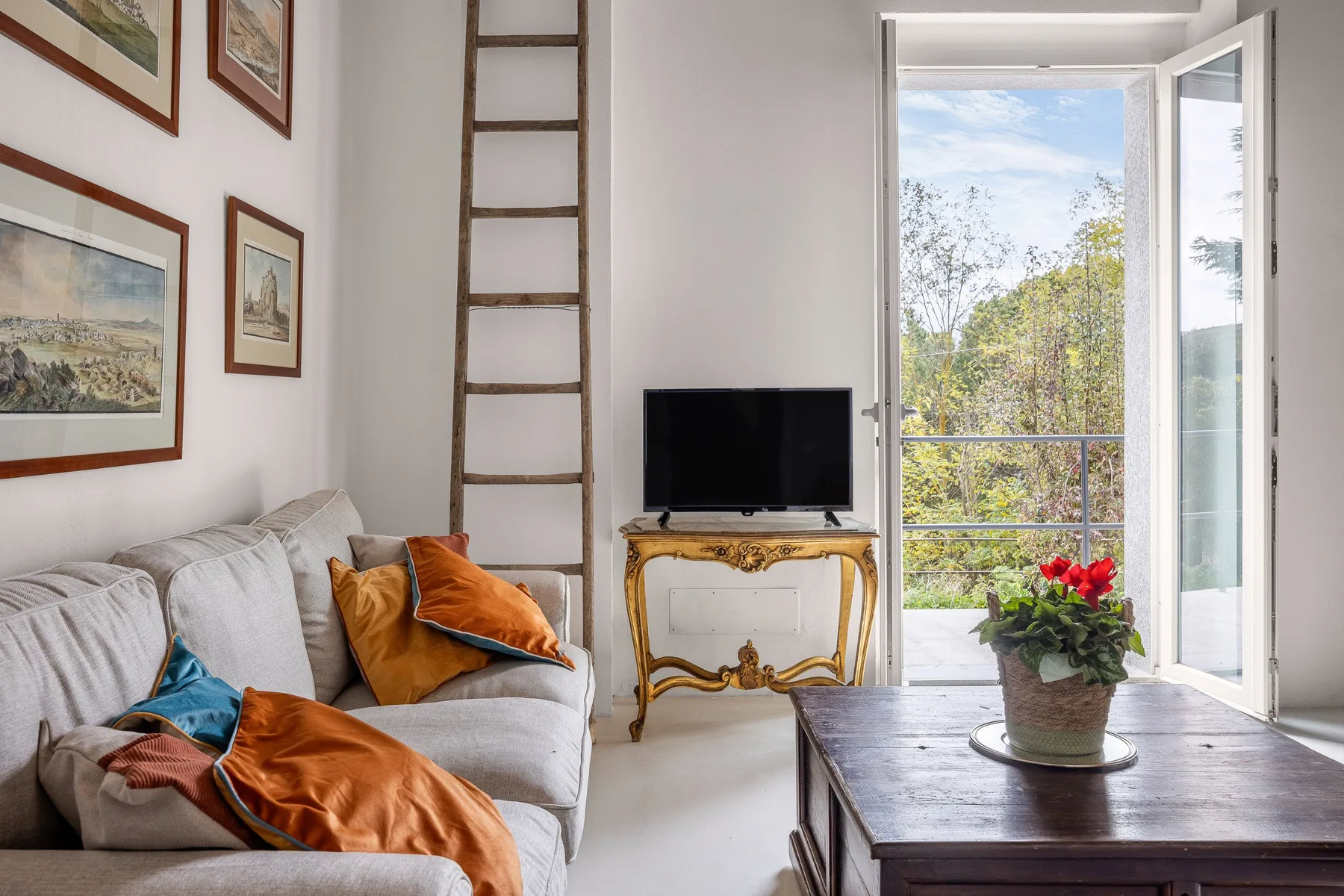 Una sala luminosa con asientos, un televisor y una puerta abierta hacia la vegetación.