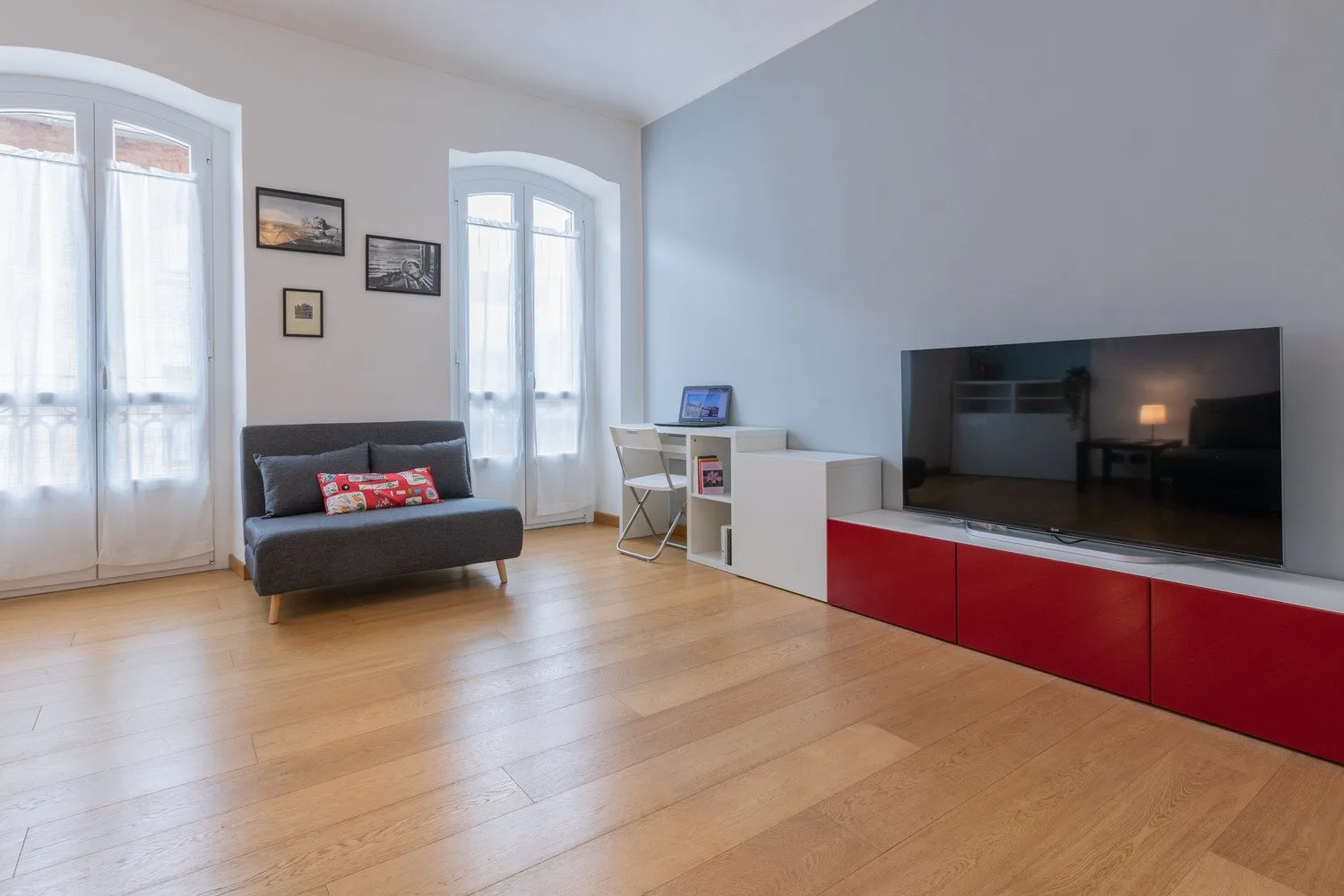 Una sala luminosa con un sofá oscuro y un televisor sobre un mueble rojo.