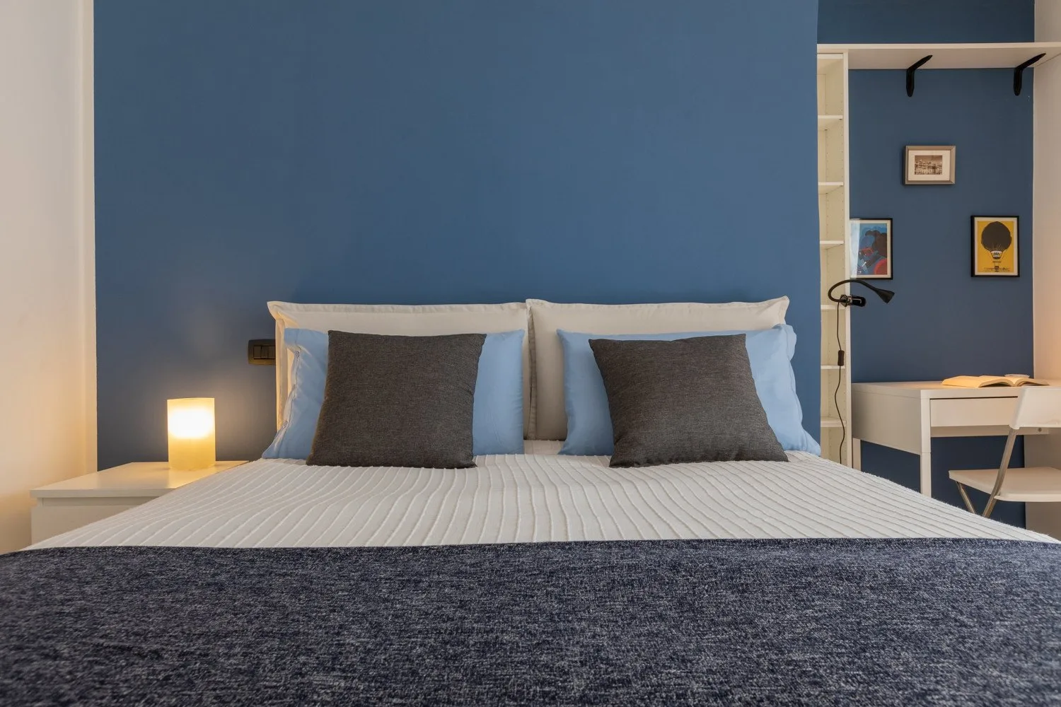 Un dormitorio con una cama bien tendida frente a una pared azul.