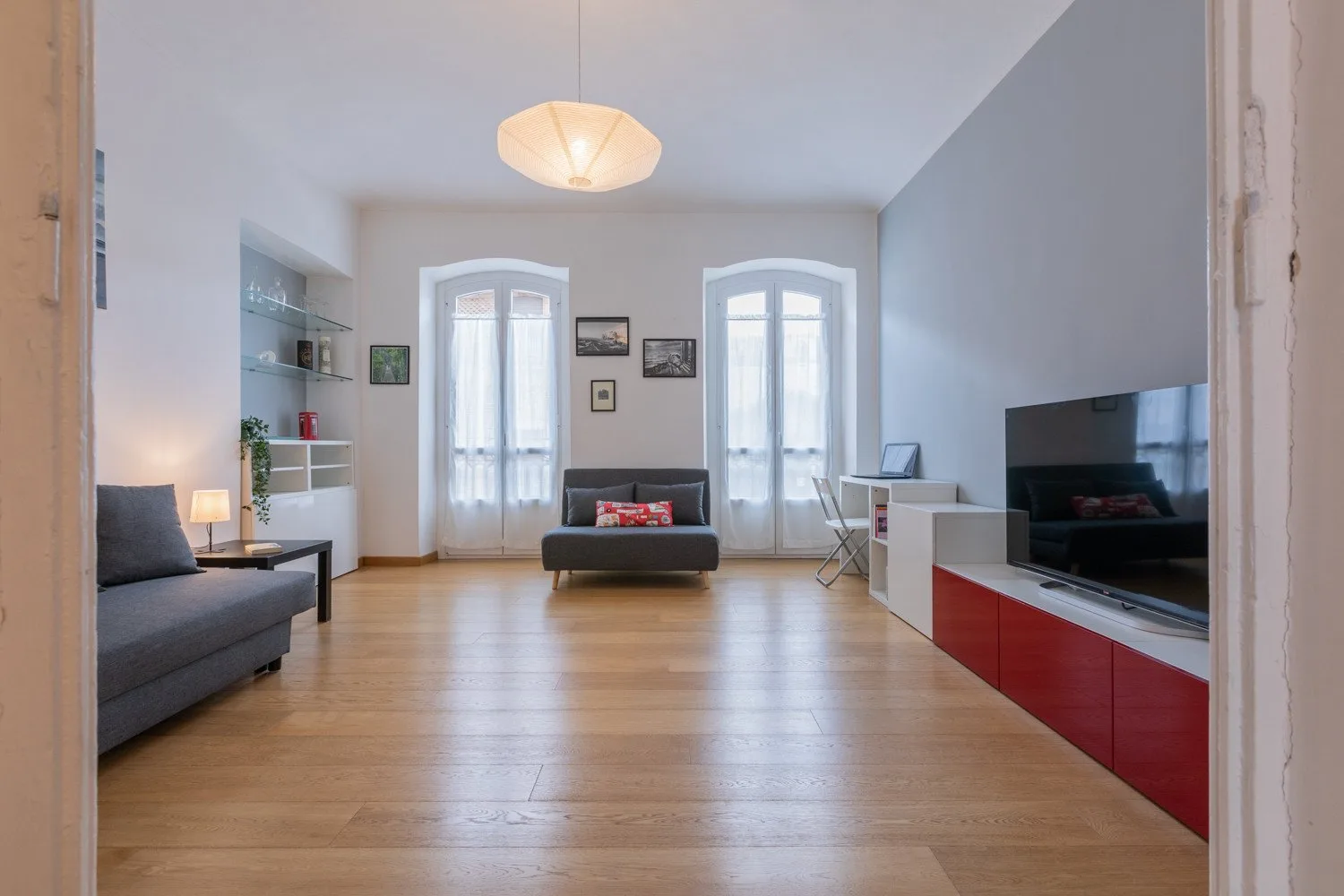 Una sala de estar con asientos, ventanas altas y un televisor.
