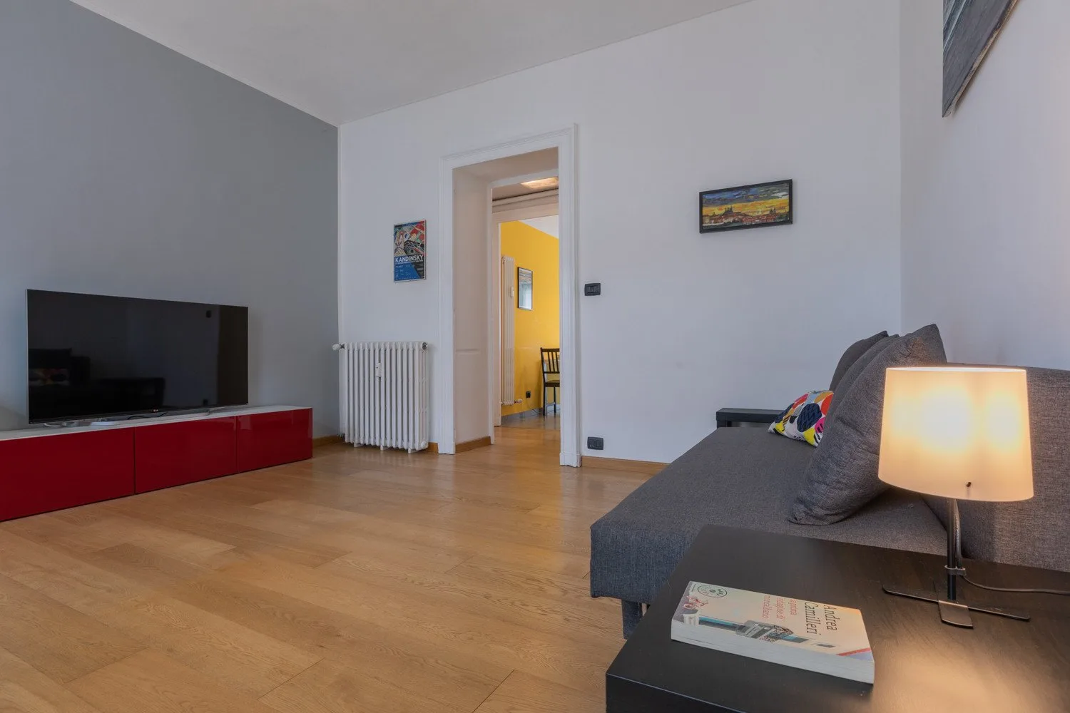 Una sala de estar con un televisor sobre un mueble rojo y un sofá gris.