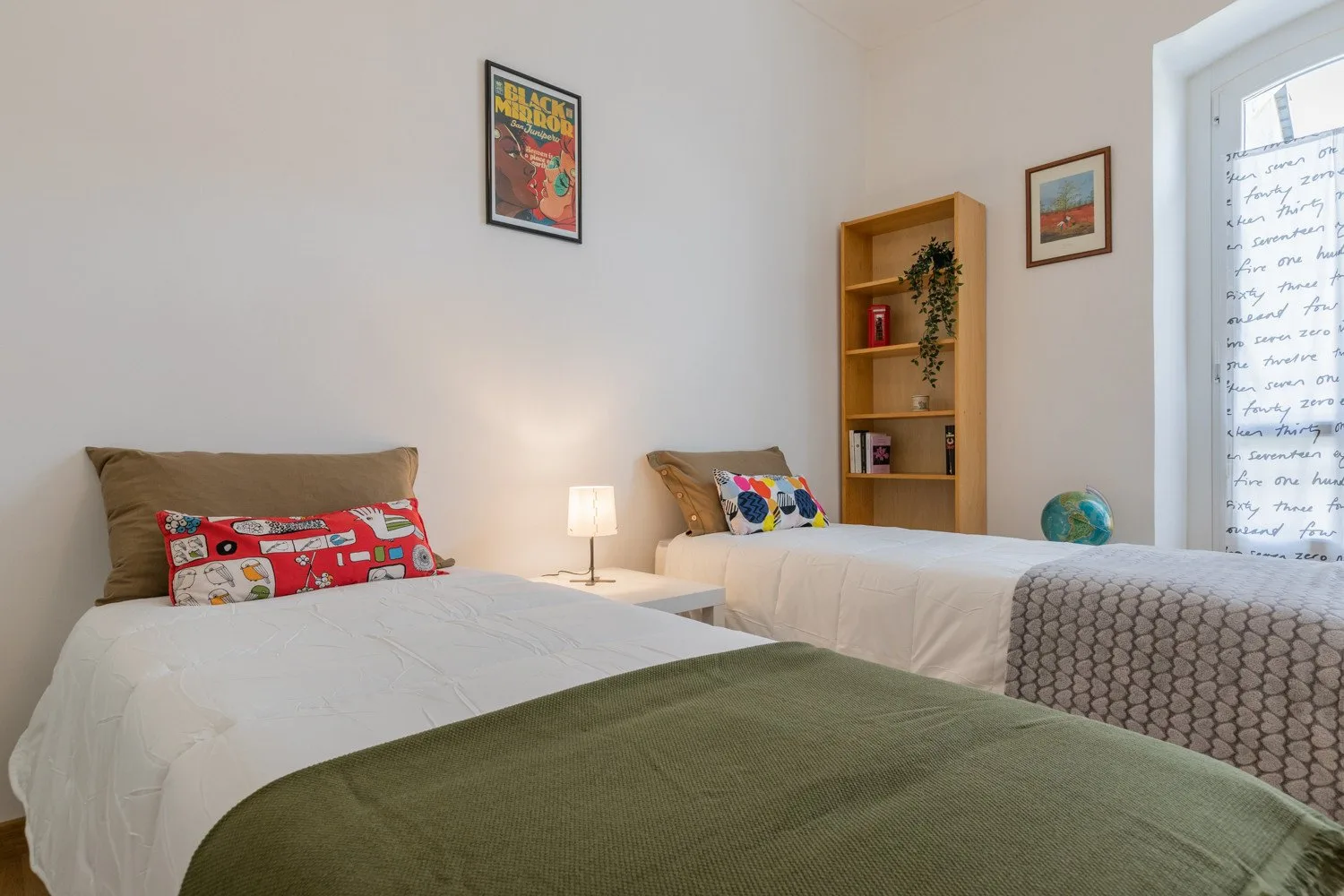 Un dormitorio con dos camas, una pequeña mesa de noche y una estantería.