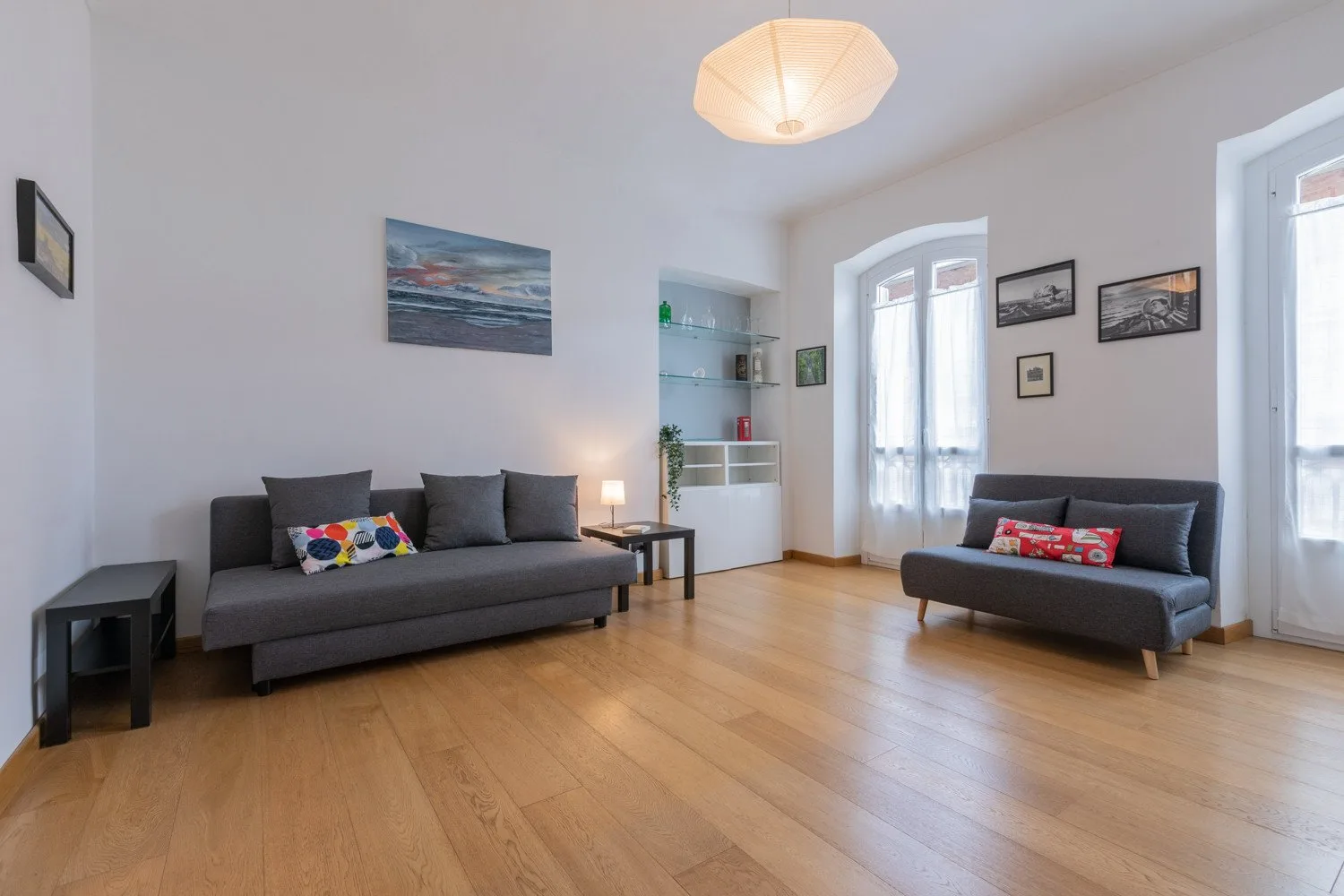 Una sala luminosa con asientos oscuros, suelo de madera y ventanas altas.