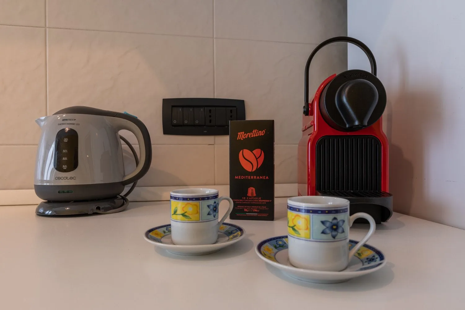Una cafetera, un hervidor y dos tazas están juntos sobre una encimera.