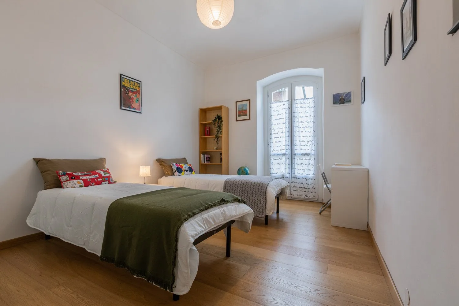 Un dormitorio luminoso con dos camas y una ventana alta.