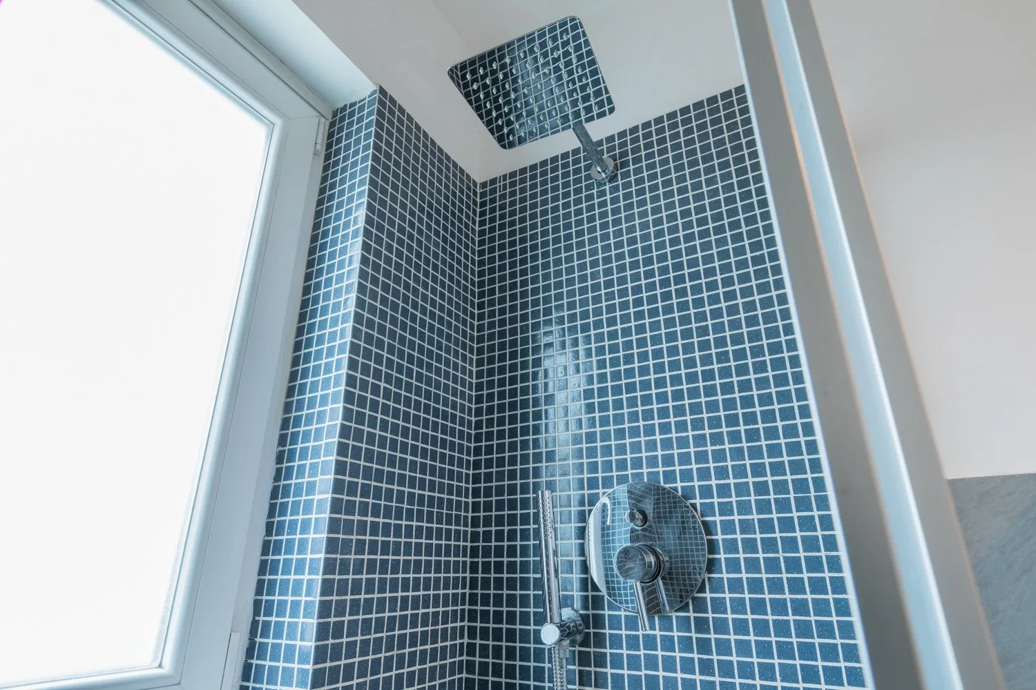 Una ducha alicatada con un cabezal de pared junto a una ventana.