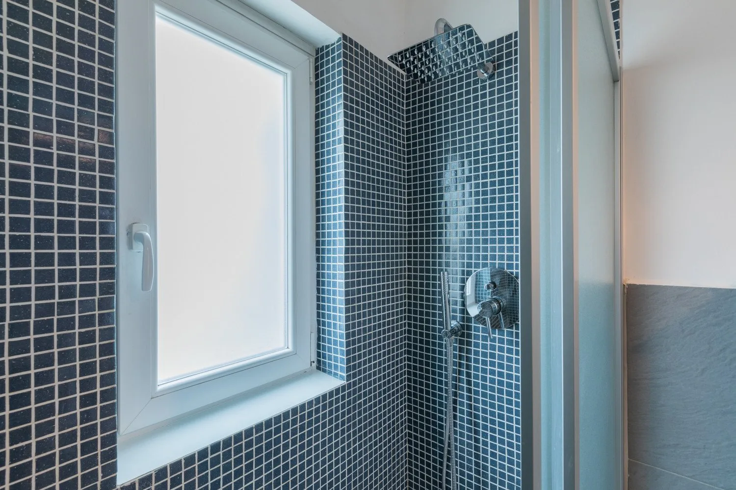 Una zona de ducha con azulejos junto a una ventana translúcida.