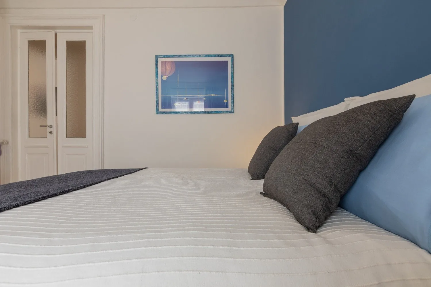Un dormitorio con una cama bien tendida y almohadas oscuras junto a una pared azul.