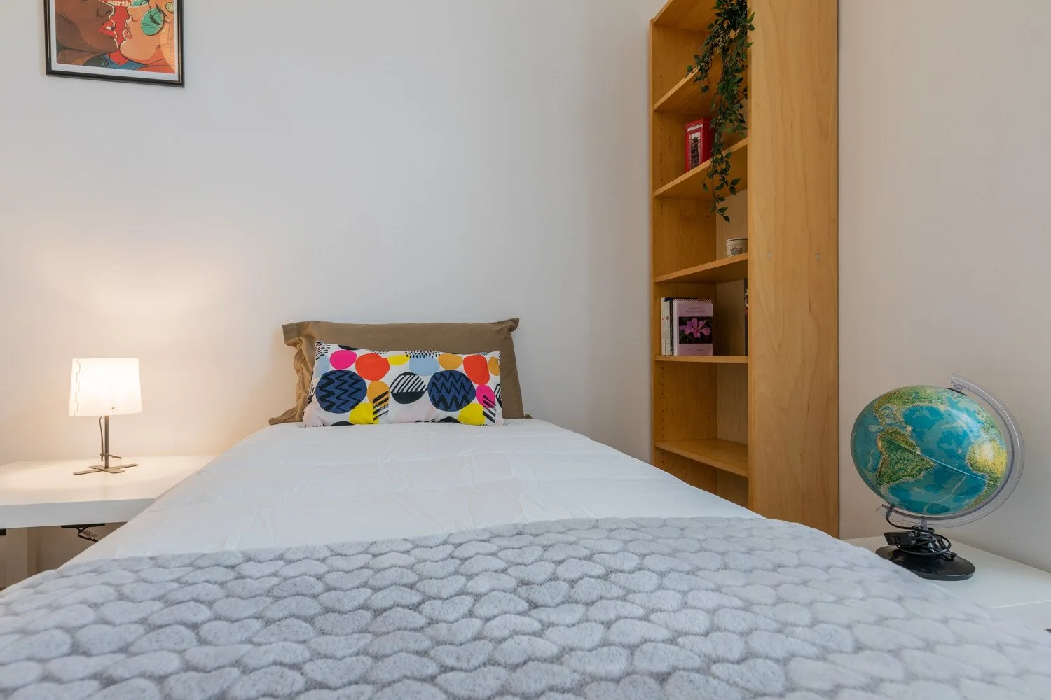 Un dormitorio con una cama bien tendida, una lámpara de noche y estanterías de madera.