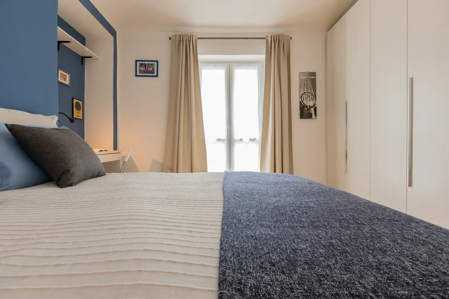 Un dormitorio con una cama, cortinas beige y una puerta acristalada luminosa.