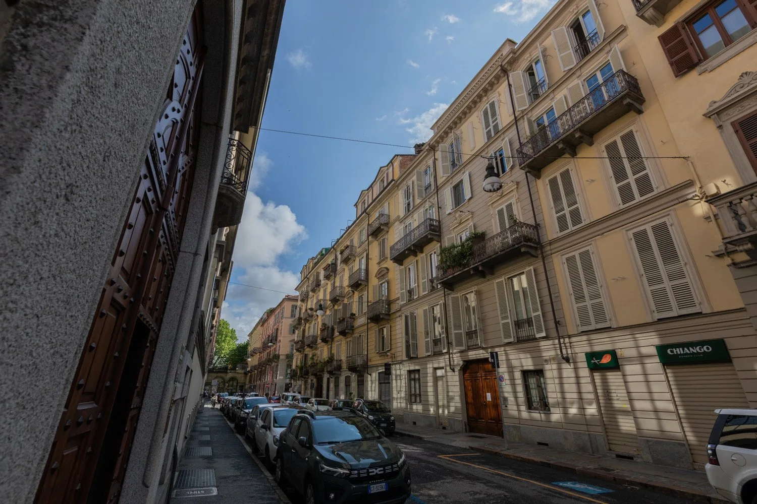 Una calle estrecha de la ciudad, flanqueada por edificios de apartamentos y coches aparcados.