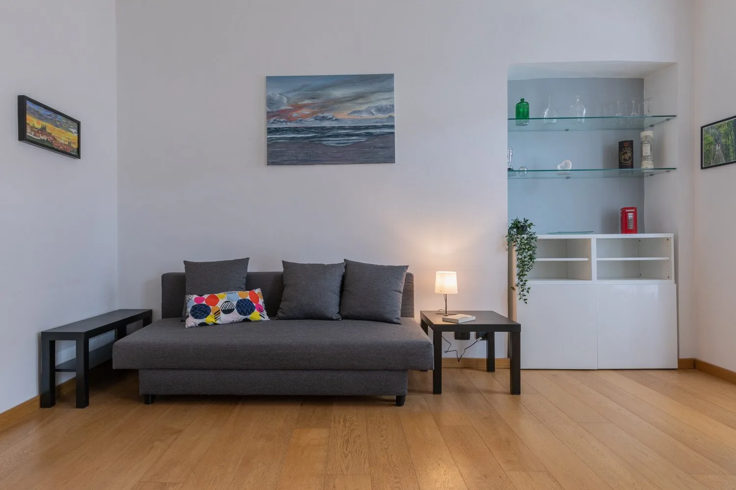 Una sala de estar con un sofá gris, mesas auxiliares y estanterías empotradas.