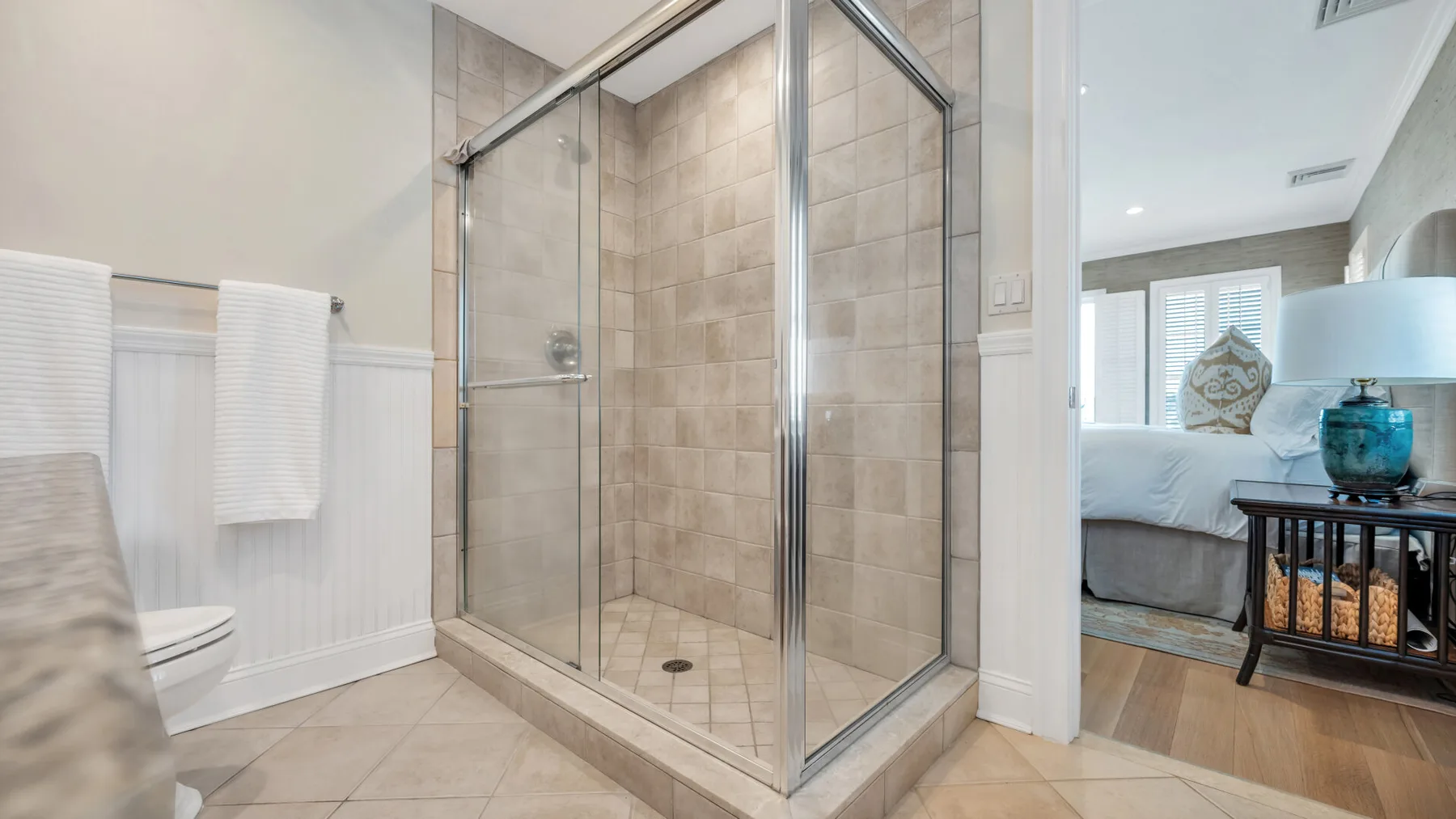 Un baño con azulejos y una ducha de vidrio junto a un dormitorio.