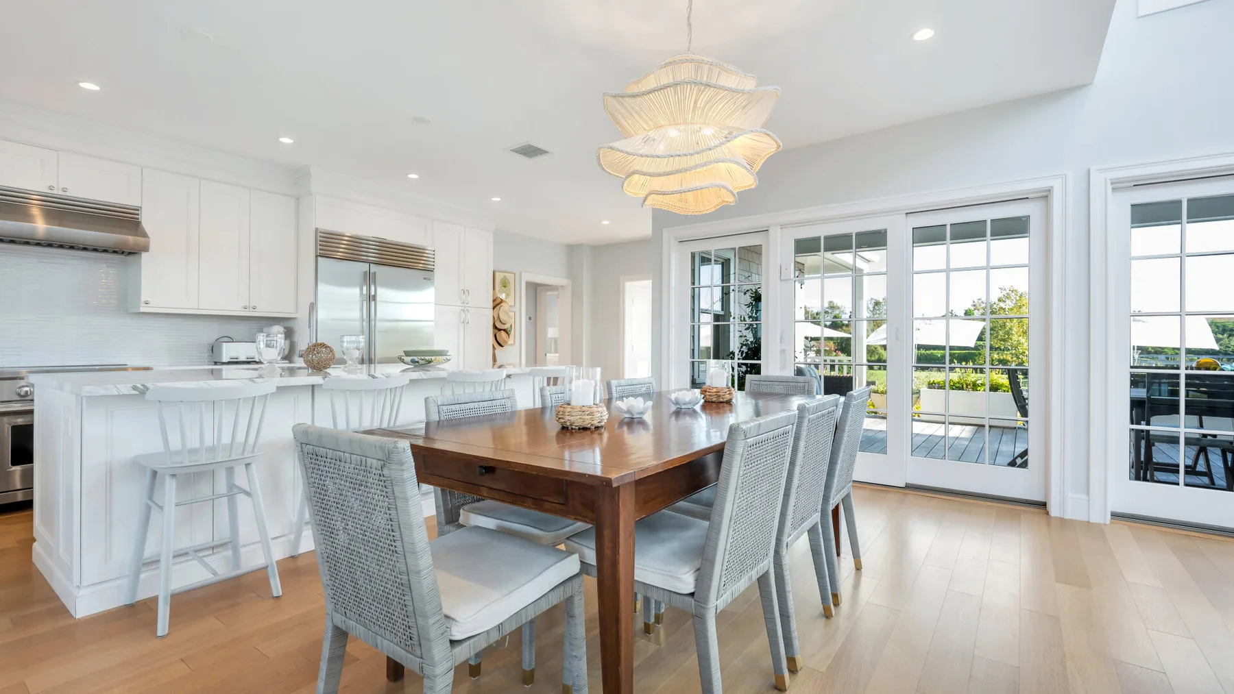 Un comedor luminoso tiene una mesa de madera y asientos junto a grandes ventanas.