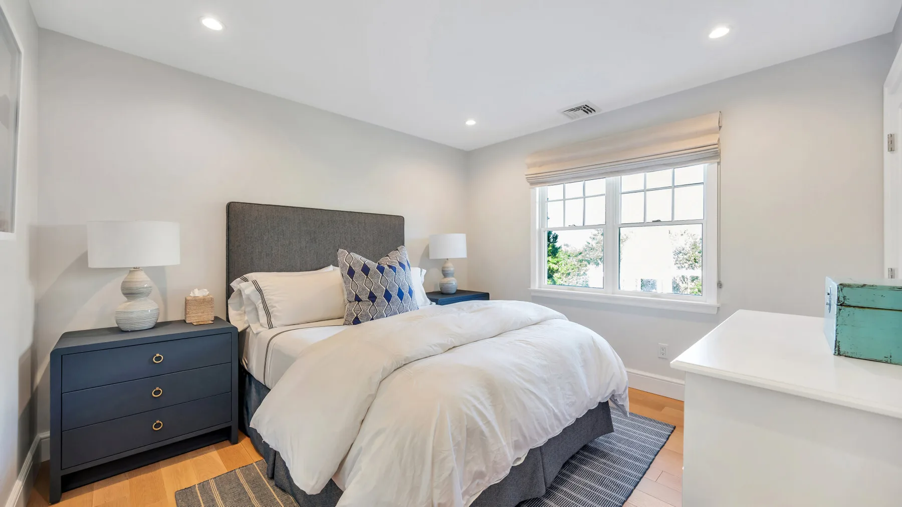 Un dormitorio luminoso con una cama bien tendida y una ventana grande.
