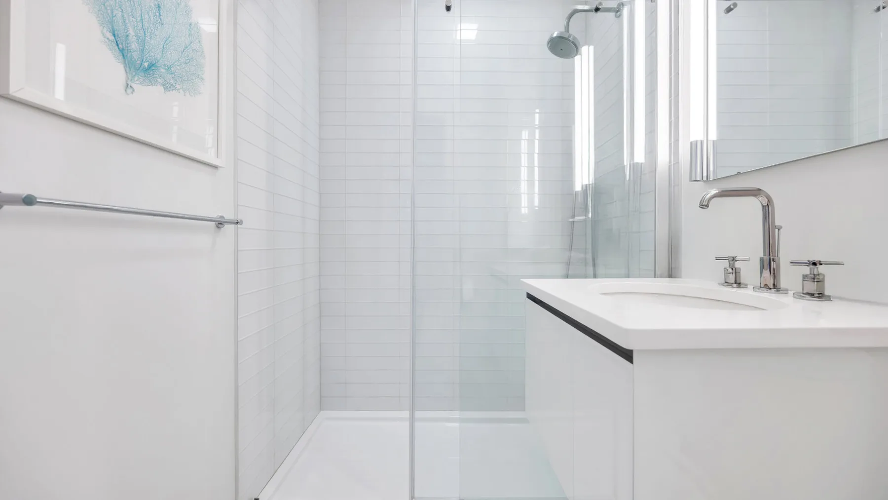 Un baño luminoso con una ducha de vidrio y un lavabo blanco.