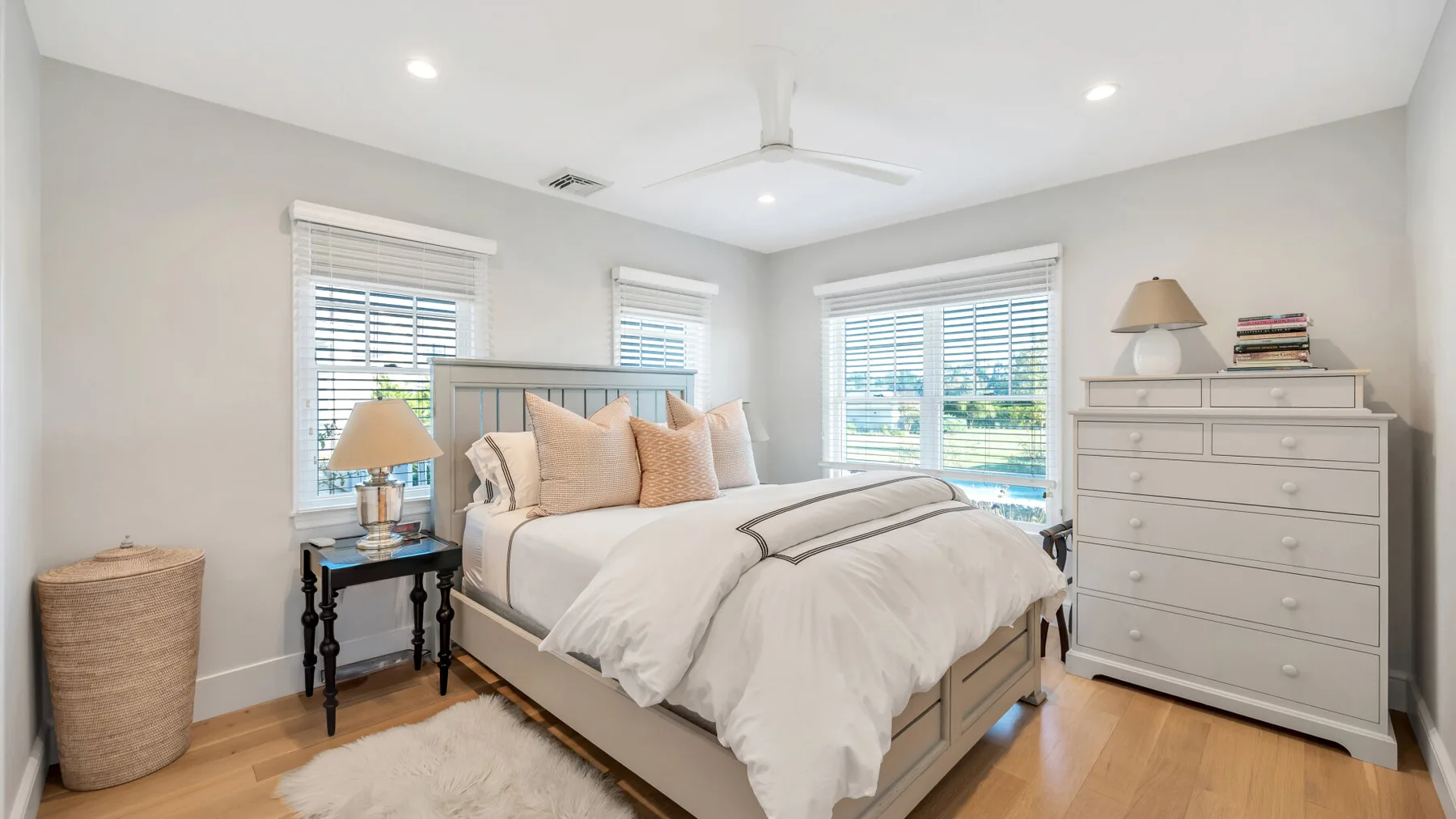 Un dormitorio luminoso con una cama bien tendida y ventanas con persianas.