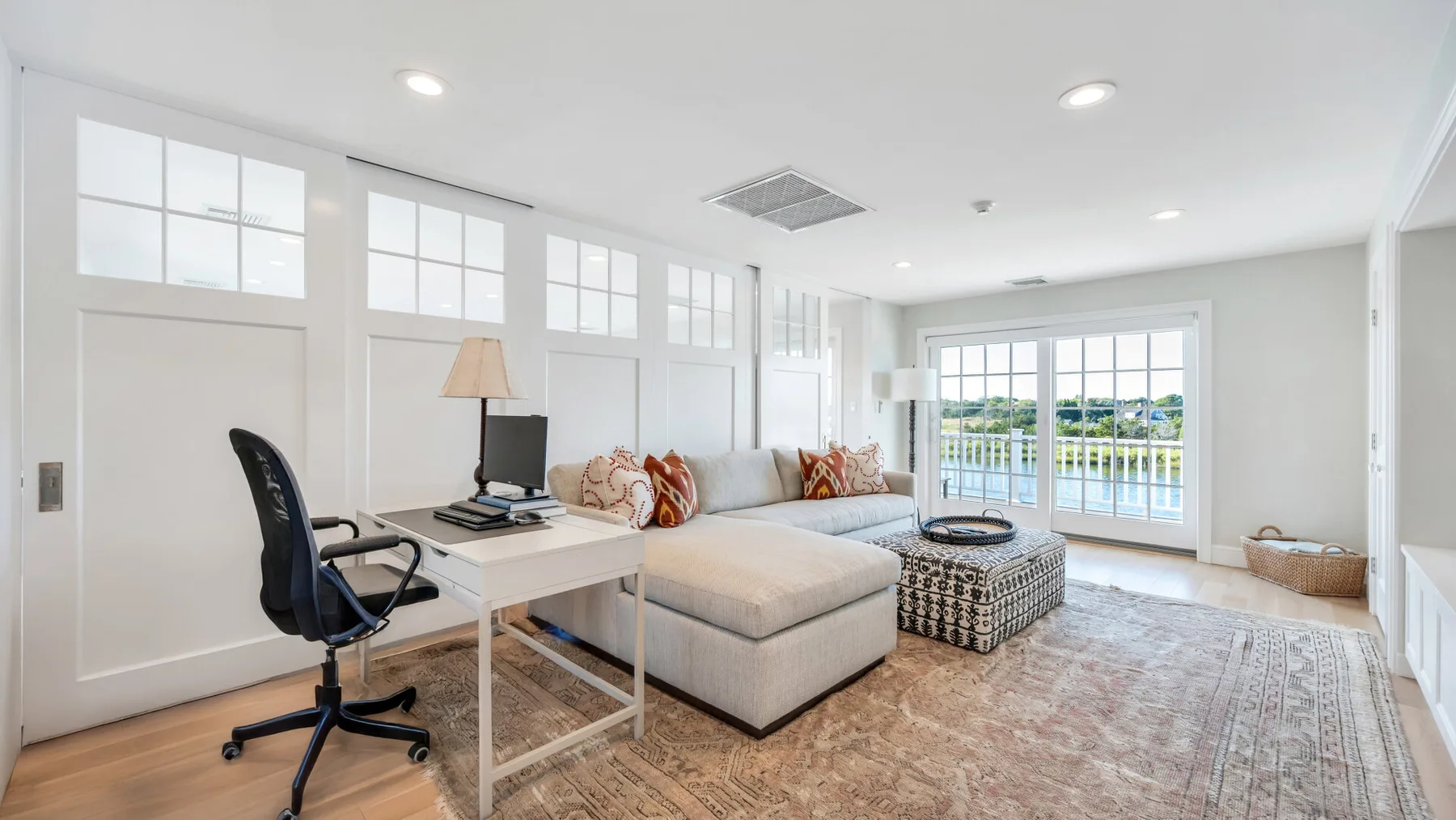 Una sala de estar luminosa con sofá seccional, escritorio y grandes ventanas.