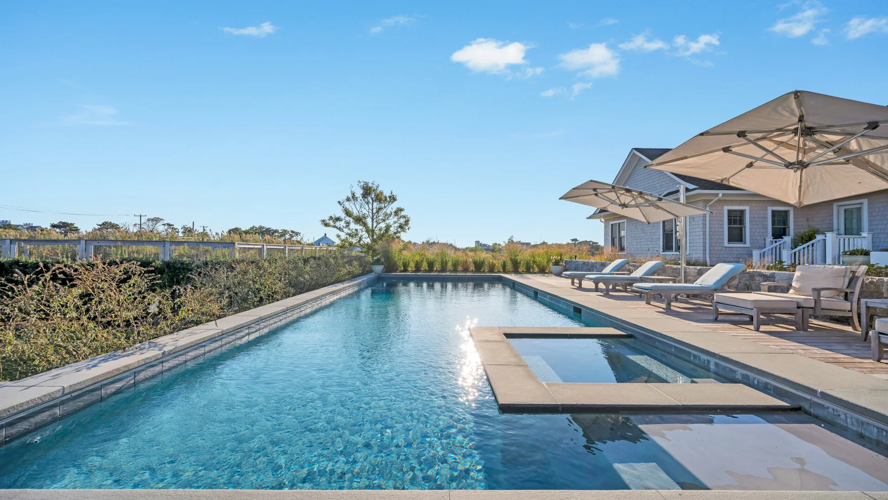 Una piscina al aire libre junto a un patio con asientos reclinables y sombrillas.