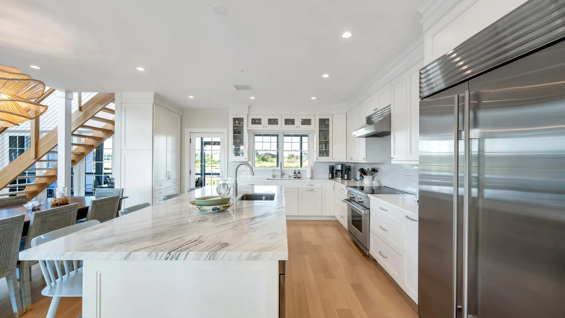 Una cocina luminosa con una gran isla, gabinetes blancos y electrodomésticos de acero inoxidable.