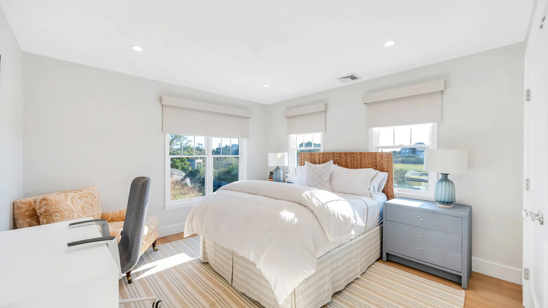 Un dormitorio luminoso con una cama, una mesita de noche y ventanas.