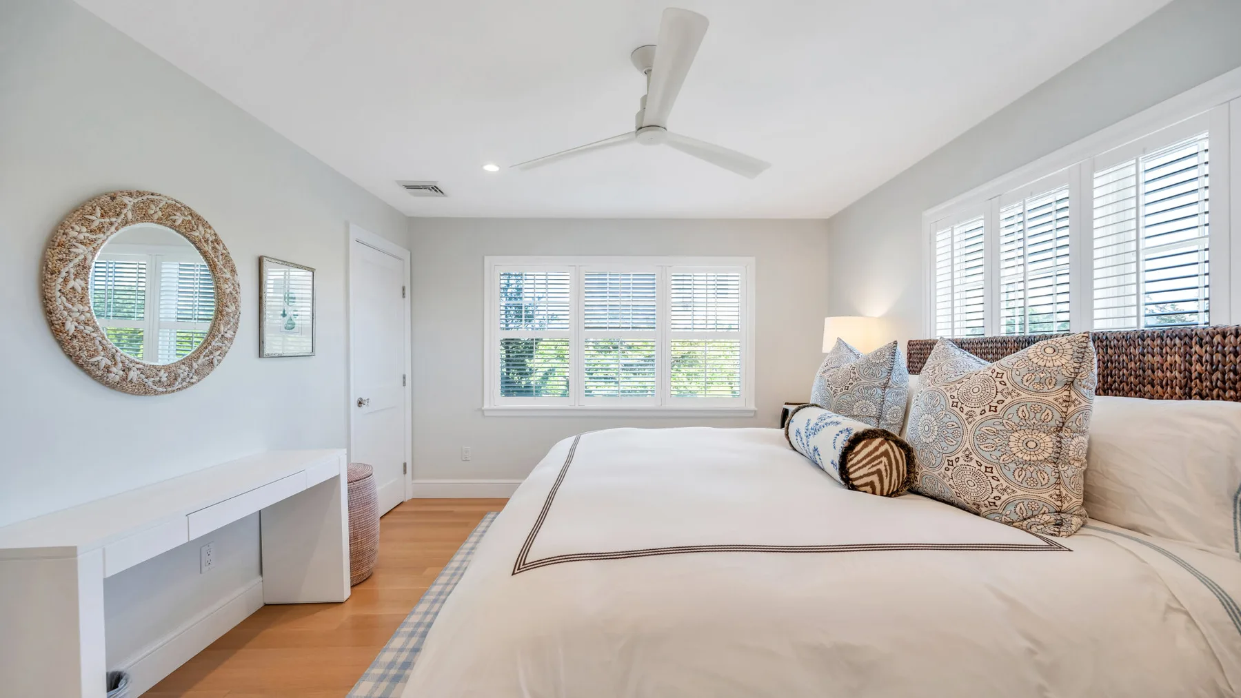 Un dormitorio luminoso con una cama grande, cojines estampados y ventanas amplias.