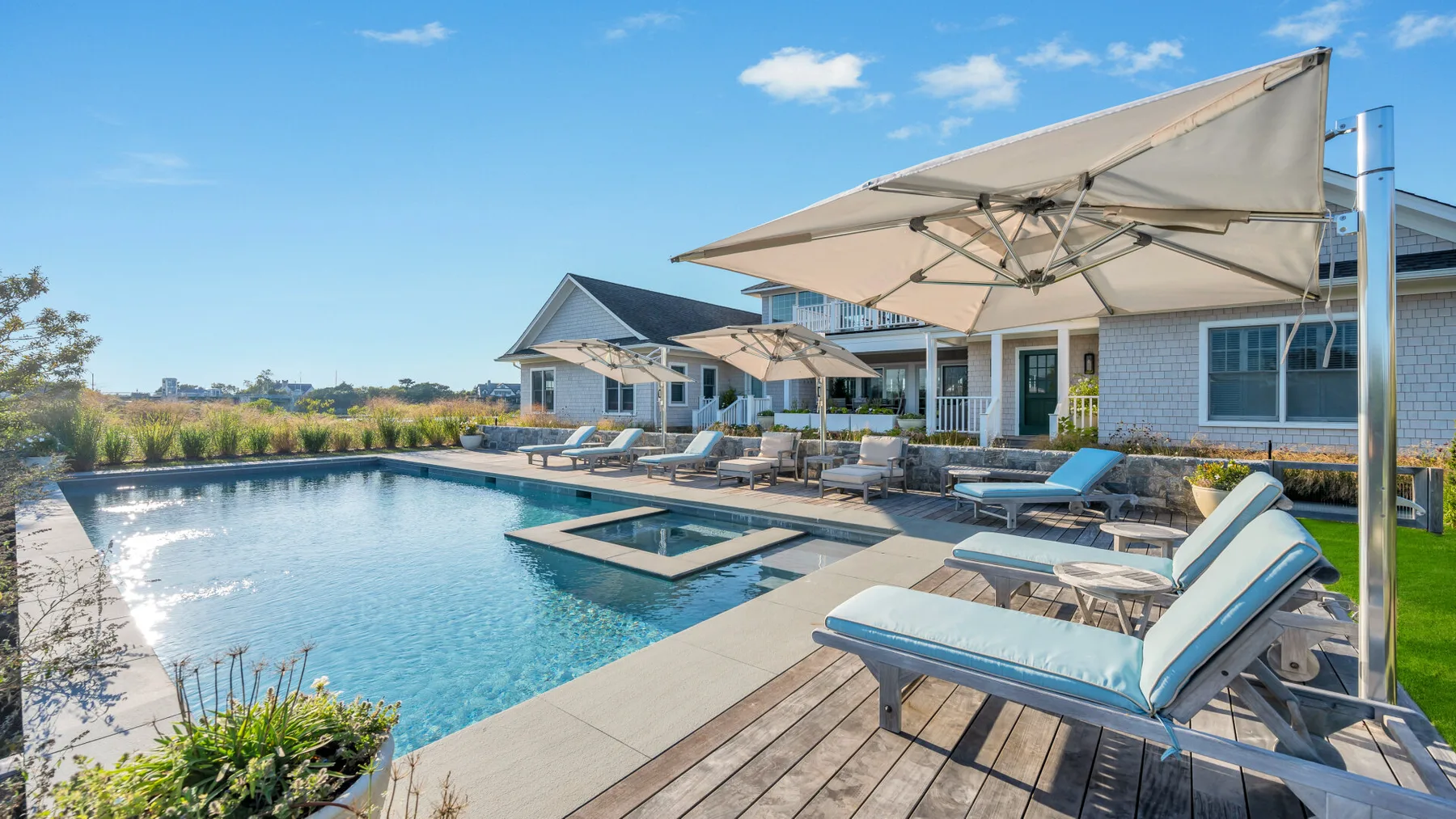 Una piscina exterior con asientos reclinables y grandes sombrillas junto a una casa moderna.