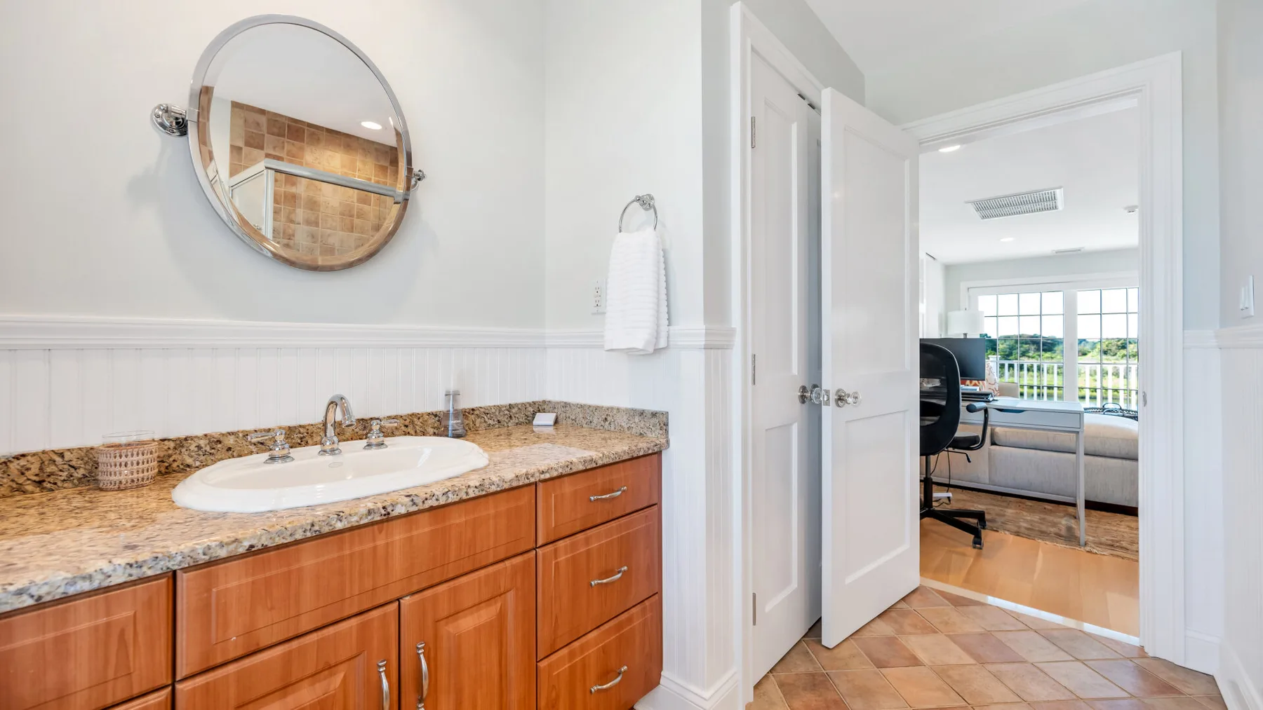 Un tocador de baño con lavabo y espejo da a una habitación luminosa.