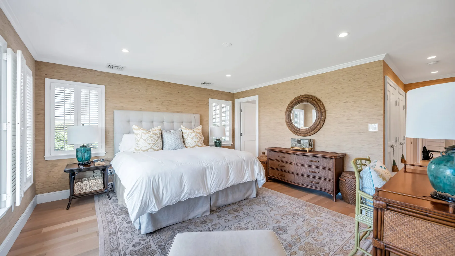 Un dormitorio luminoso con una cama, una alfombra estampada y una cómoda de madera.