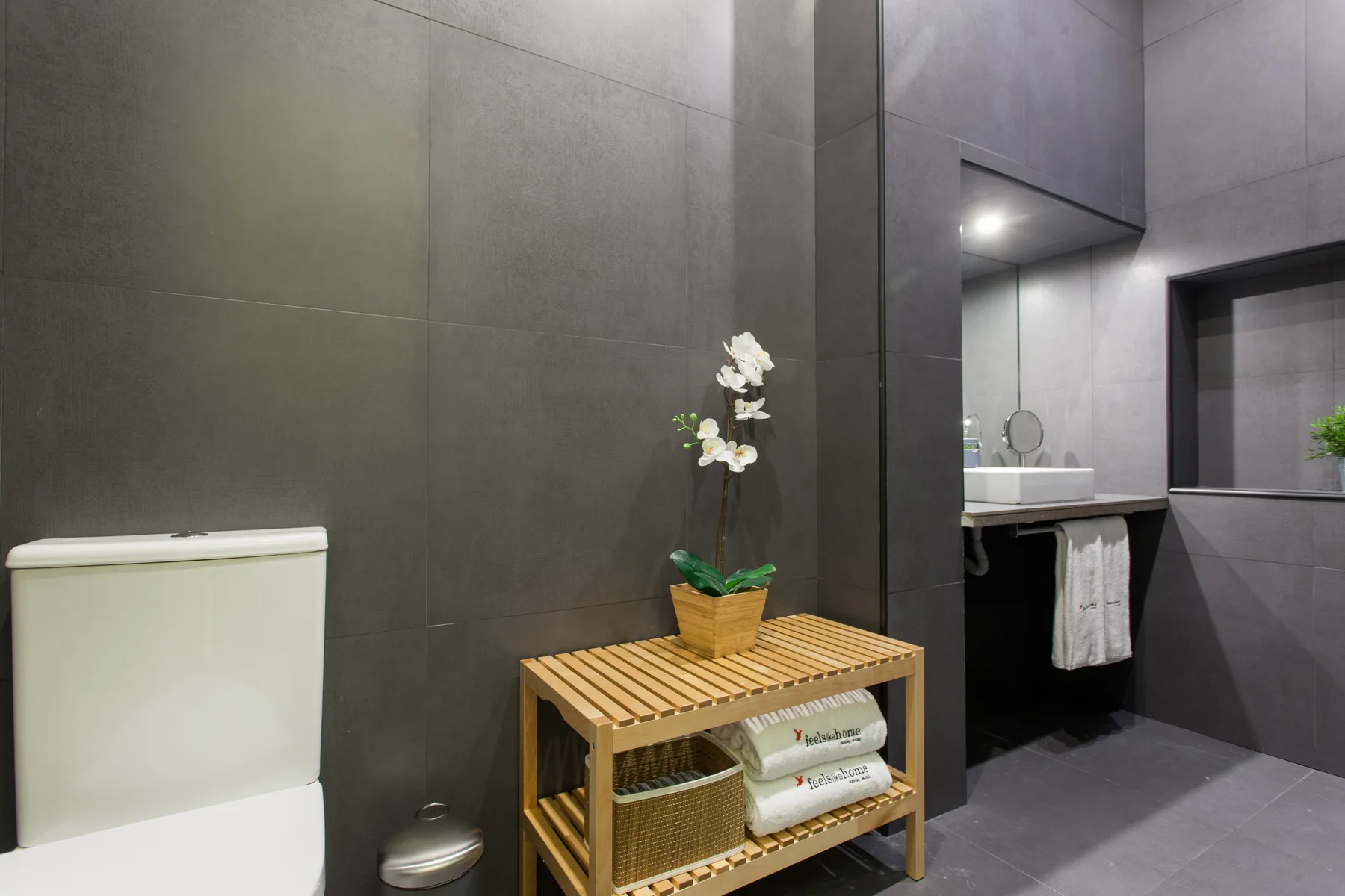 Baño con azulejos, lavabo, inodoro y un toallero de madera.