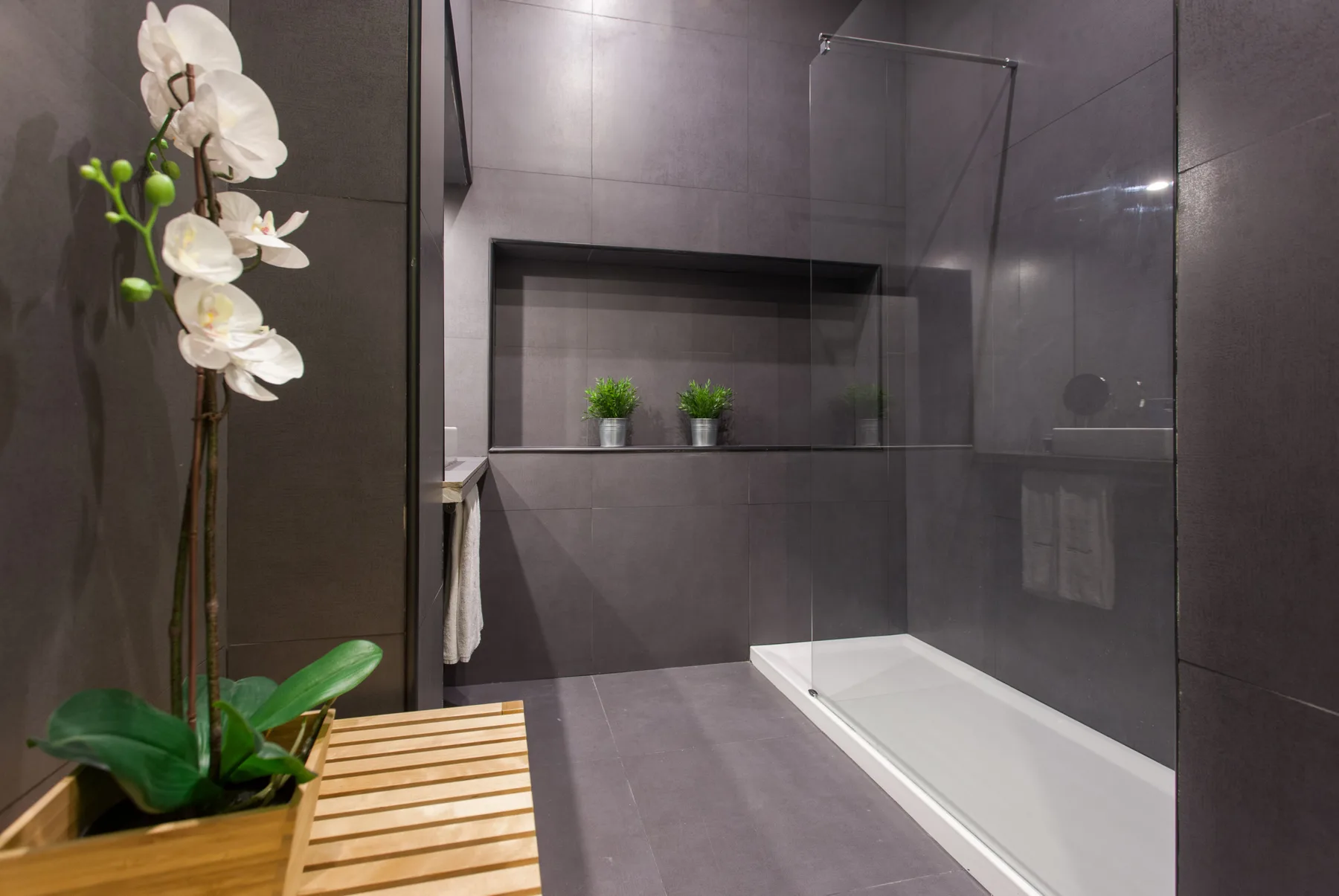 Un baño moderno con una ducha de vidrio y una orquídea blanca.