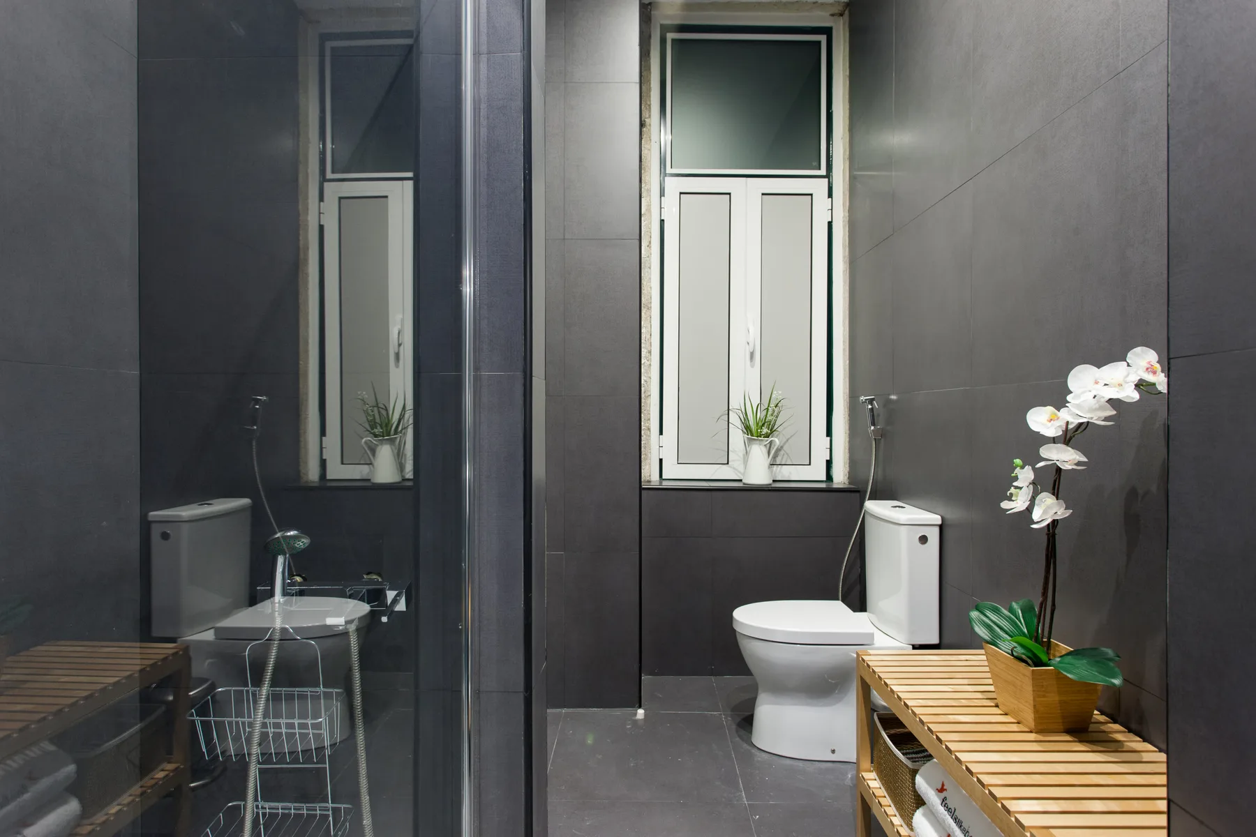 Un baño alicatado con una ventana, un inodoro y una orquídea en maceta.
