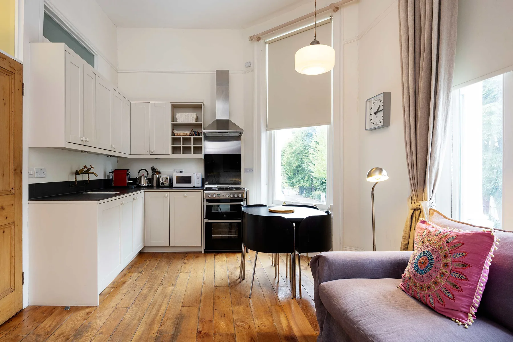 A bright open-plan kitchen and living area with a dining table beside tall windows.