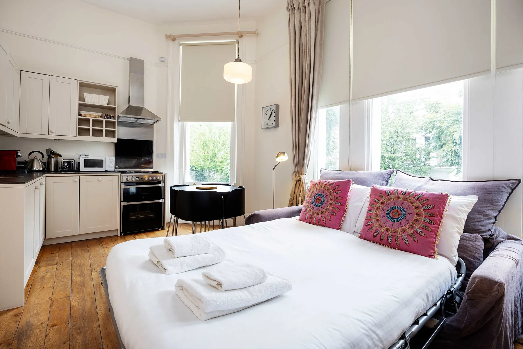 A bright bedroom with a kitchenette and a bed set beside large windows.