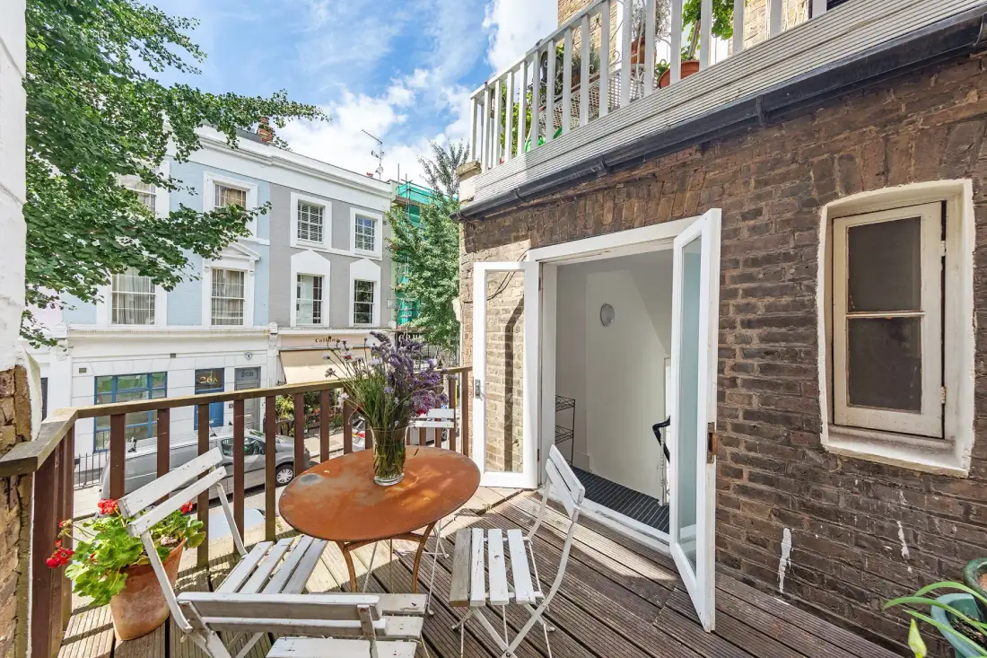 A small outdoor deck with a table and seating beside an open doorway.