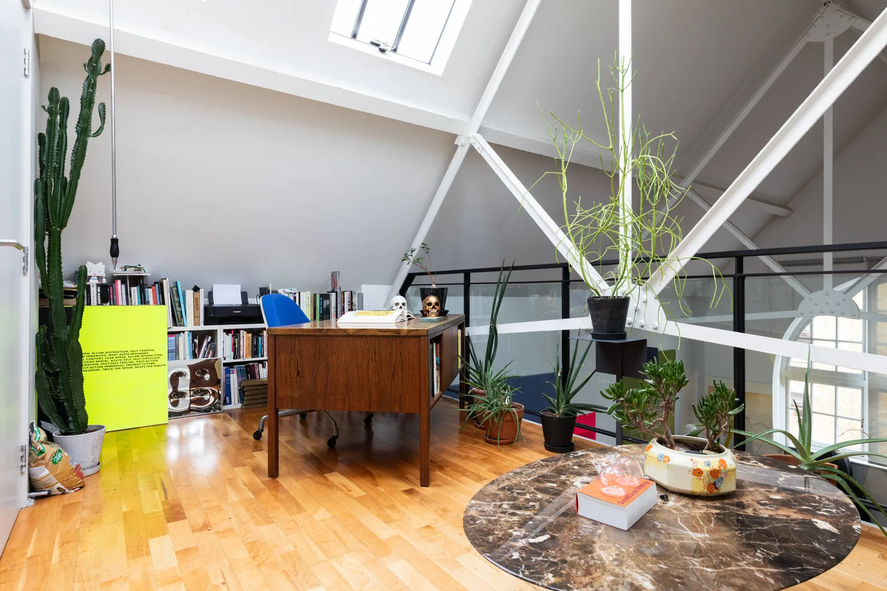 Una oficina luminosa tipo loft con un escritorio de madera, estanterías y plantas.
