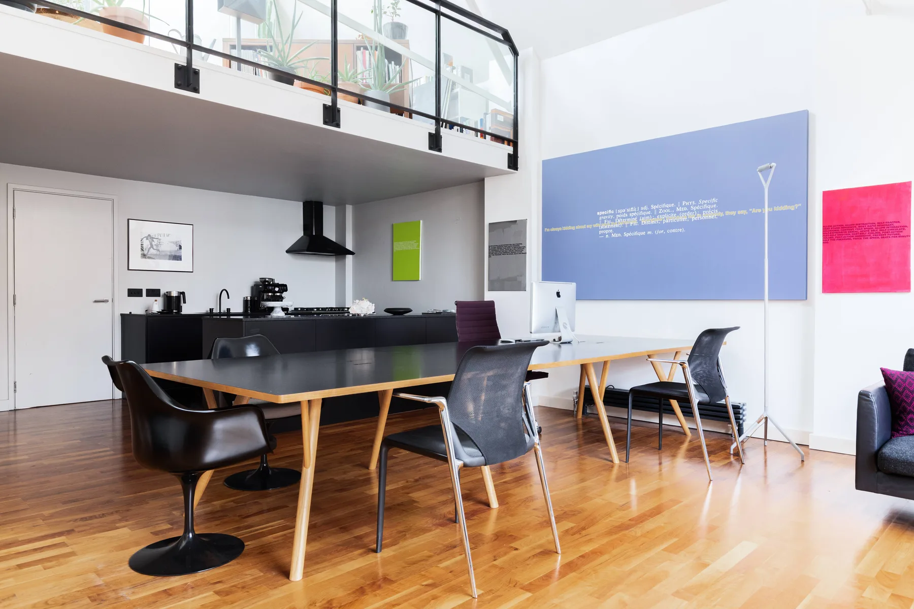 Un luminoso comedor tipo loft con una mesa larga y sillas bajo un altillo con barandilla de vidrio.