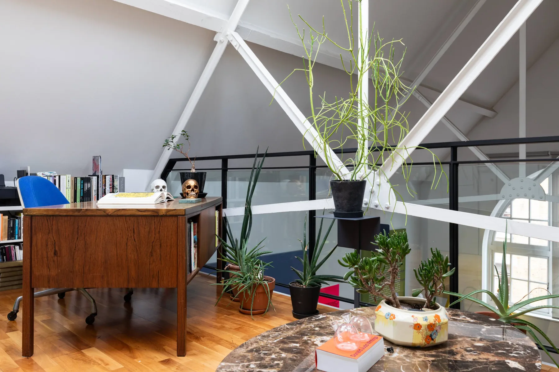 Un luminoso interior tipo loft con un escritorio de madera, plantas y una barandilla de vidrio.