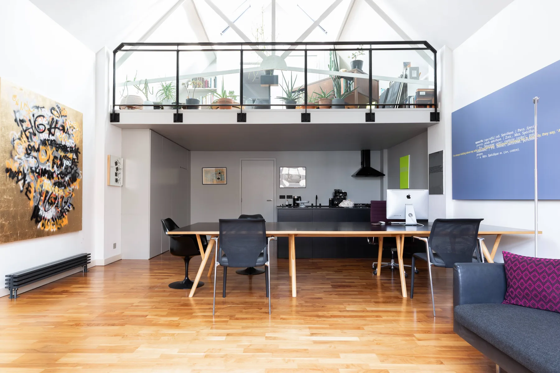 Una luminosa sala-comedor de planta abierta con cocina bajo un altillo con barandilla de vidrio.