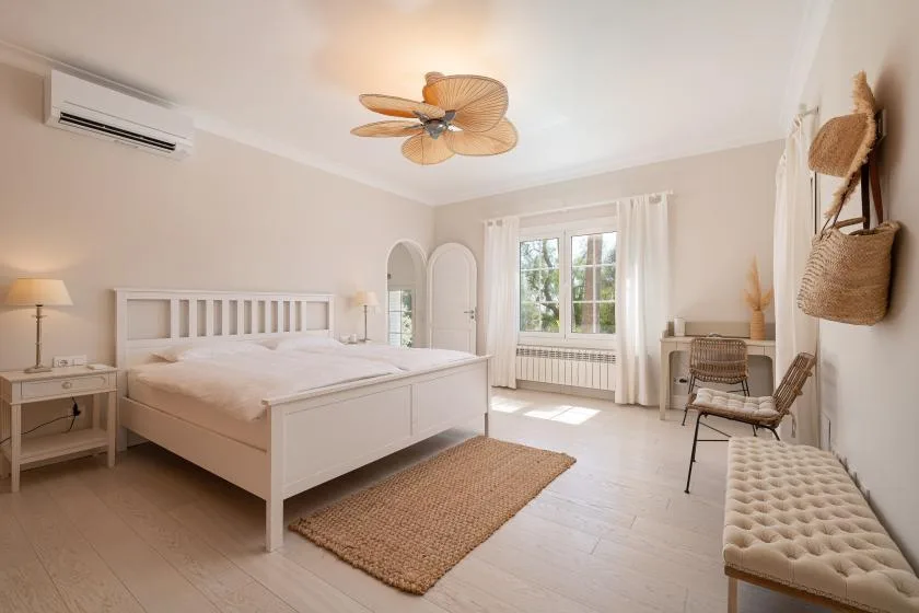 A bright bedroom with a bed, a window, and a woven rug.